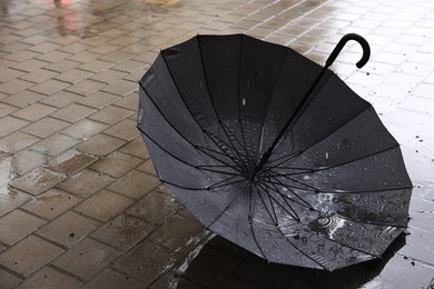 Photo of Black umbrella on wet asphalt under heavy rain, closeup. Space for text