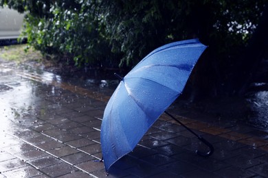 Photo of Blue umbrella on wet asphalt under heavy rain, space for text