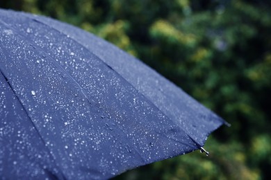 Photo of Blue umbrella under heavy rain outdoors, closeup