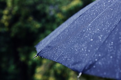 Photo of Blue umbrella under heavy rain outdoors, closeup. Space for text