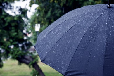 Photo of Blue umbrella under heavy rain outdoors, closeup. Space for text