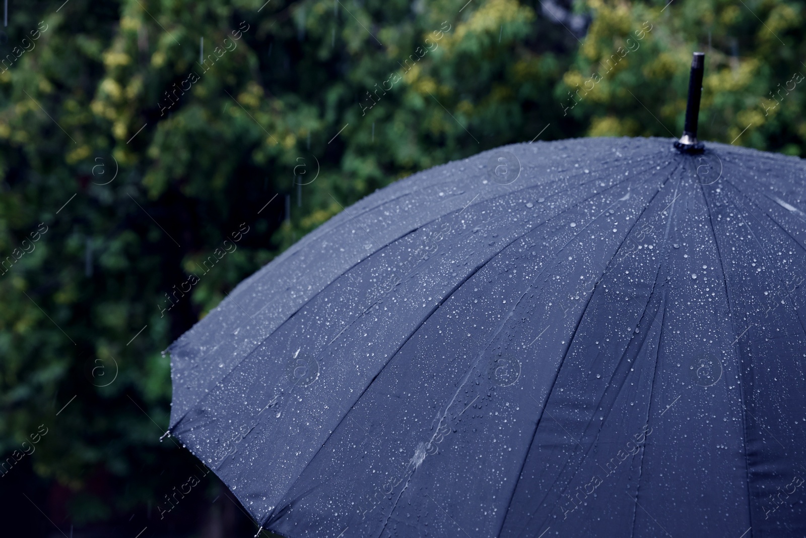 Photo of Blue umbrella under heavy rain outdoors, closeup