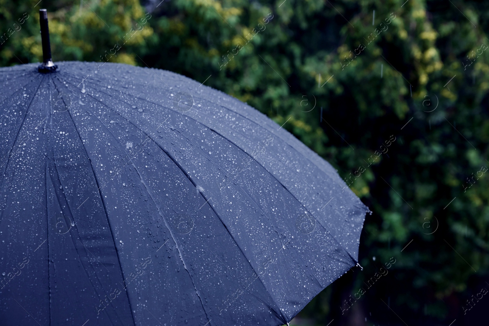 Photo of Blue umbrella under heavy rain outdoors, closeup. Space for text