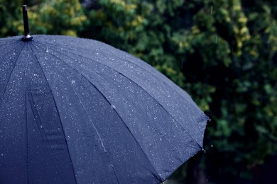 Photo of Blue umbrella under heavy rain outdoors, closeup. Space for text