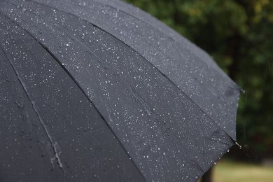 Photo of Black umbrella under heavy rain outdoors, closeup