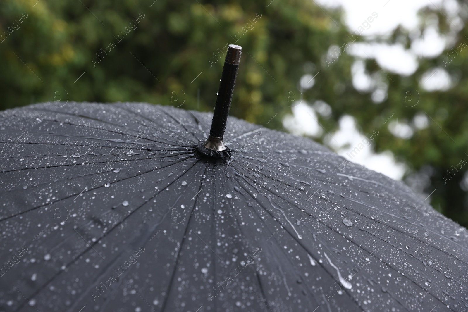 Photo of Black umbrella under heavy rain outdoors, closeup