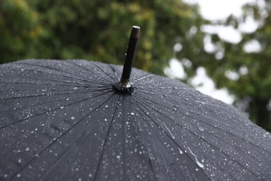 Photo of Black umbrella under heavy rain outdoors, closeup