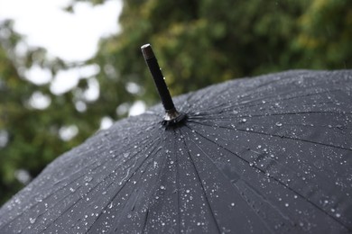 Photo of Black umbrella under heavy rain outdoors, closeup