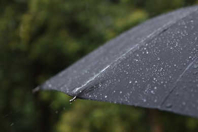 Photo of Black umbrella under heavy rain outdoors, closeup