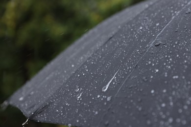 Photo of Black umbrella under heavy rain outdoors, closeup