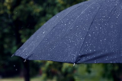 Photo of Blue umbrella under heavy rain outdoors, closeup