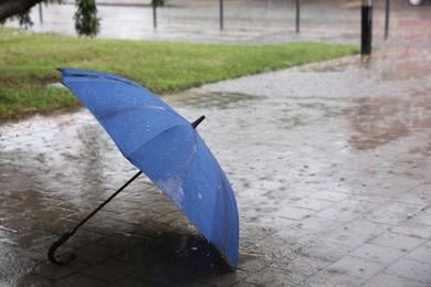 Photo of Blue umbrella on wet asphalt under heavy rain, space for text
