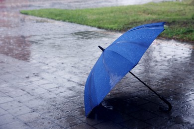 Photo of Blue umbrella on wet asphalt under heavy rain, space for text