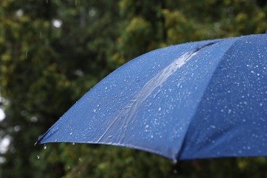 Photo of Blue umbrella under heavy rain outdoors, closeup