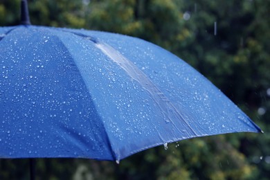 Photo of Blue umbrella under heavy rain outdoors, closeup