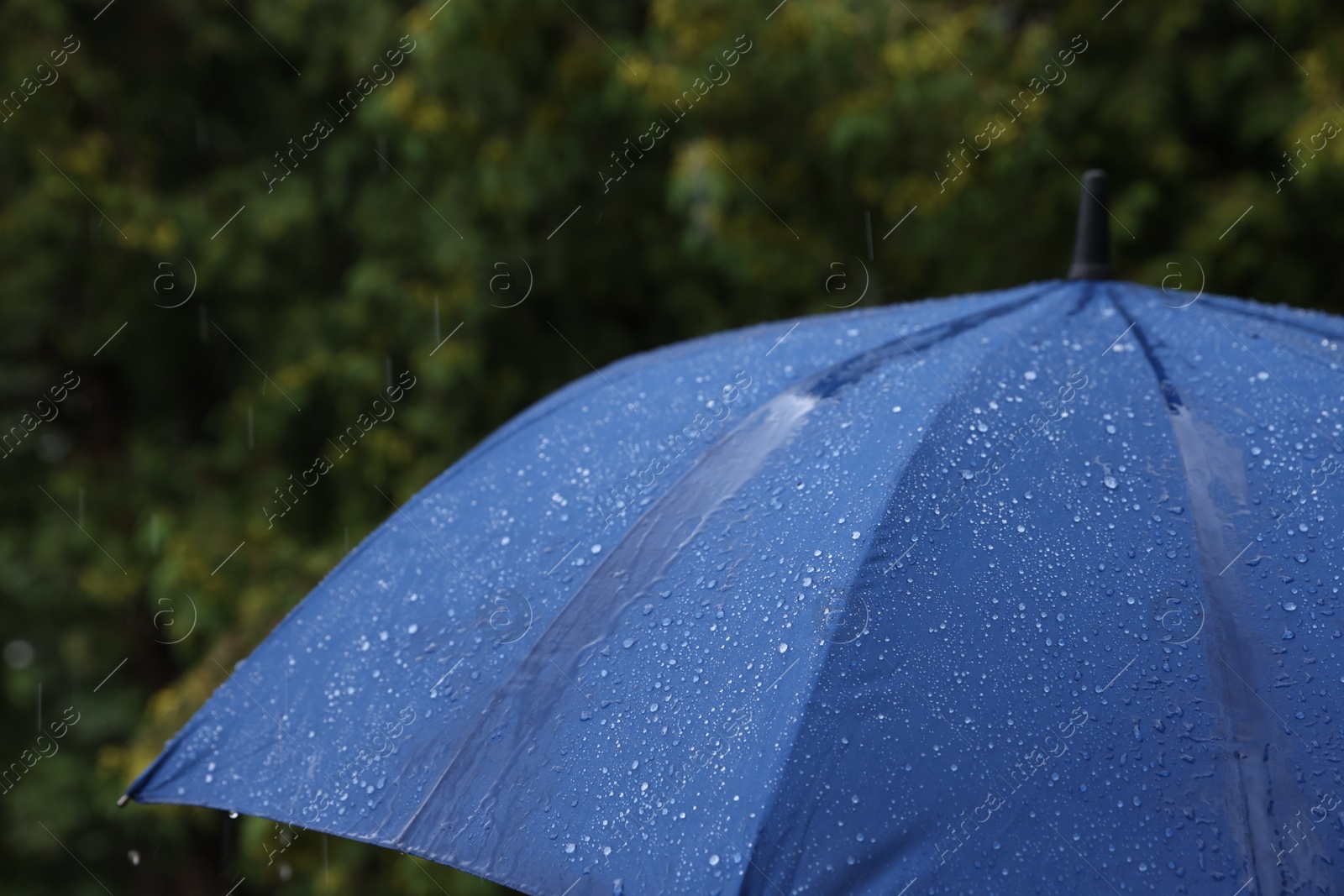 Photo of Blue umbrella under heavy rain outdoors, closeup