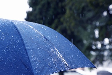 Photo of Blue umbrella under heavy rain outdoors, closeup