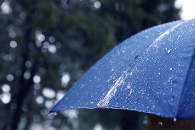 Photo of Blue umbrella under heavy rain outdoors, closeup. Space for text
