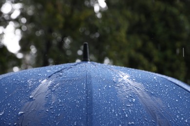 Photo of Blue umbrella under heavy rain outdoors, closeup