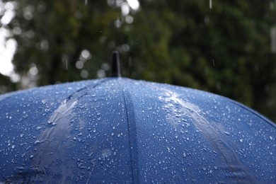 Photo of Blue umbrella under heavy rain outdoors, closeup