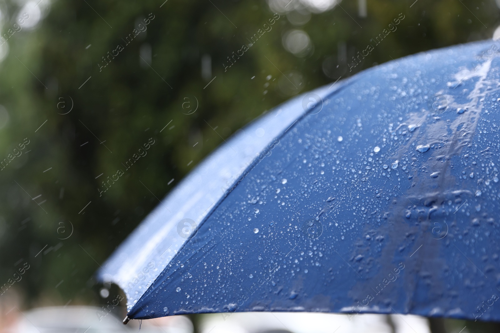 Photo of Blue umbrella under heavy rain outdoors, closeup