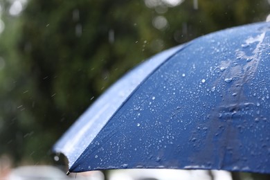 Photo of Blue umbrella under heavy rain outdoors, closeup