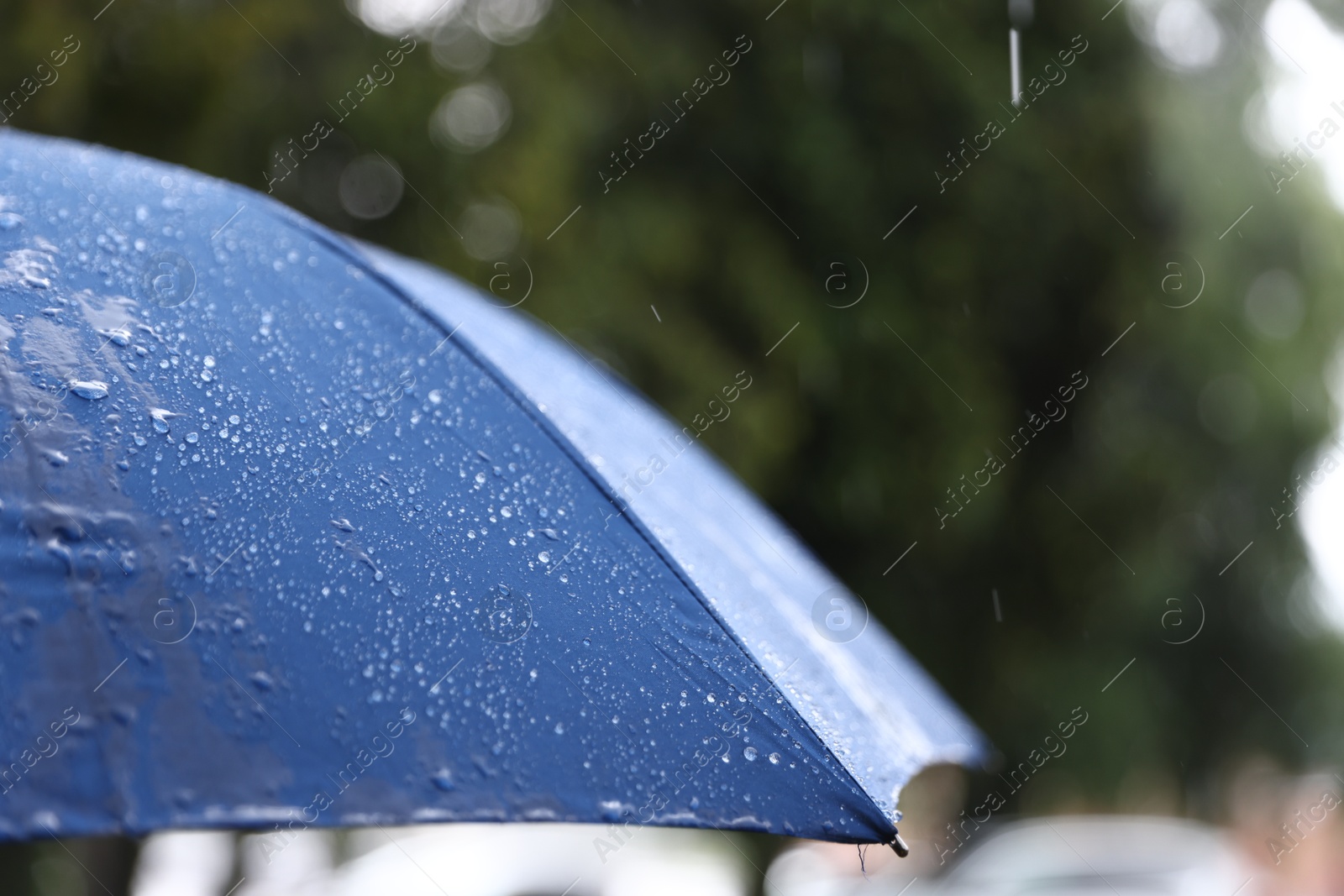 Photo of Blue umbrella under heavy rain outdoors, closeup. Space for text