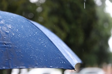 Photo of Blue umbrella under heavy rain outdoors, closeup. Space for text