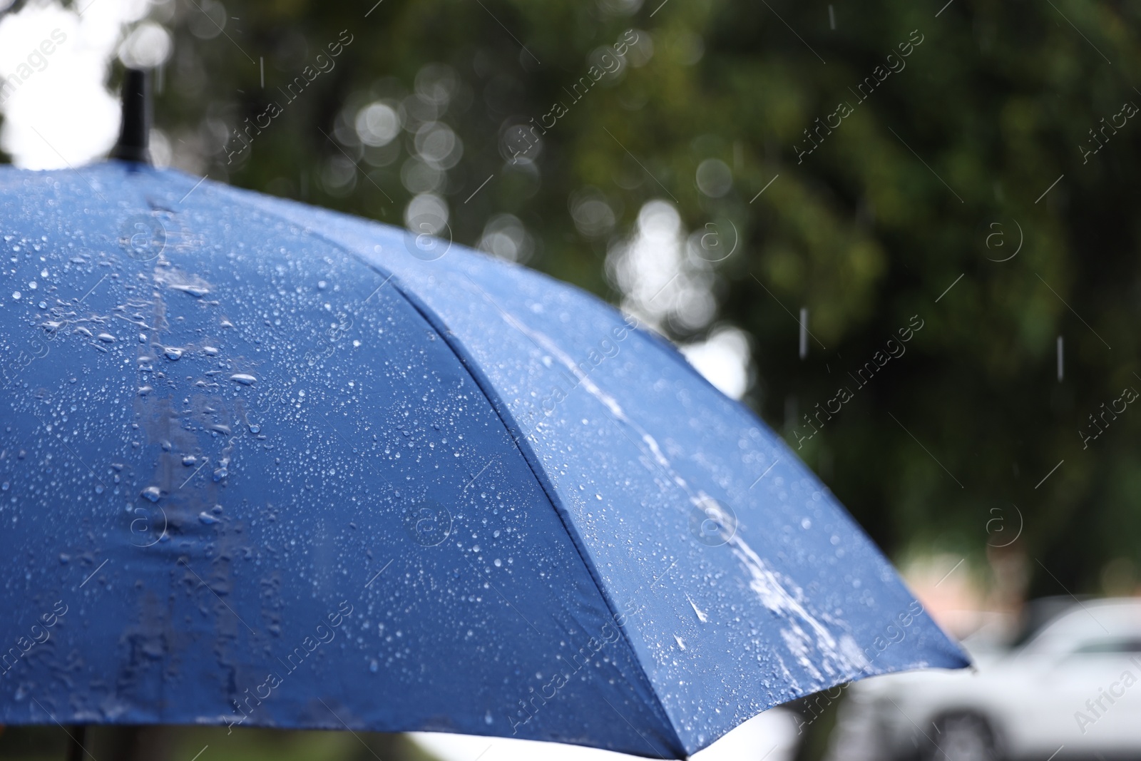 Photo of Blue umbrella under heavy rain outdoors, closeup