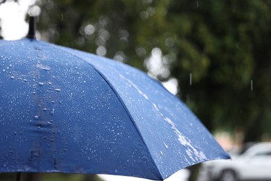 Photo of Blue umbrella under heavy rain outdoors, closeup