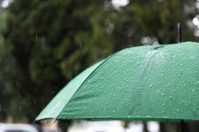 Photo of Green umbrella under heavy rain outdoors, closeup