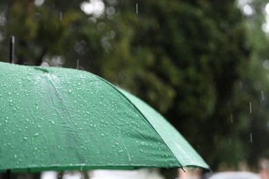 Photo of Green umbrella under heavy rain outdoors, closeup