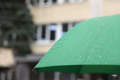 Photo of Green umbrella under heavy rain outdoors, closeup. Space for text