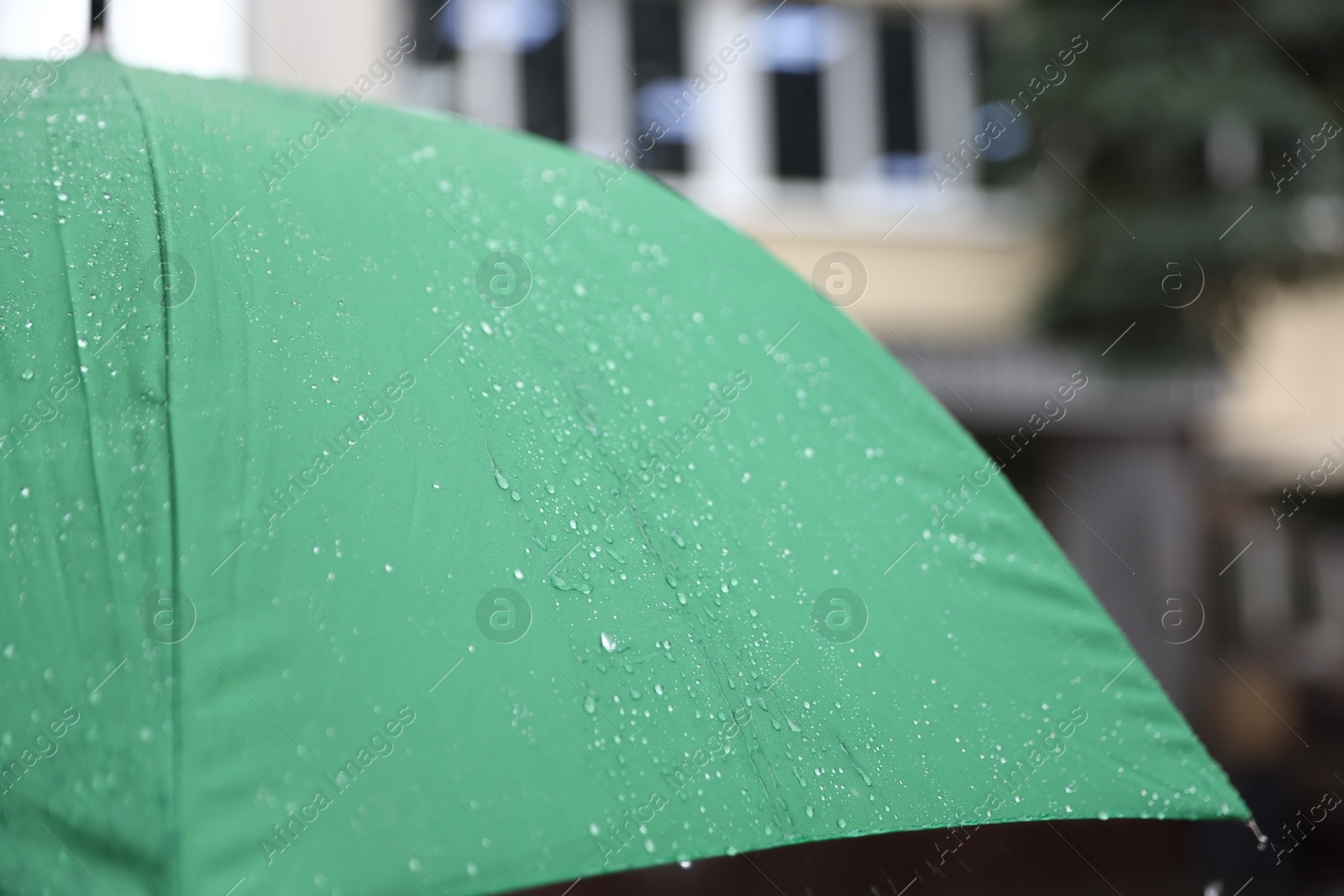 Photo of Green umbrella under heavy rain outdoors, closeup