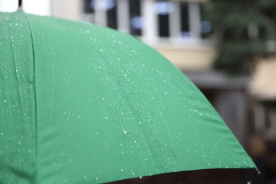 Photo of Green umbrella under heavy rain outdoors, closeup