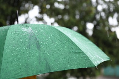 Photo of Green umbrella under heavy rain outdoors, closeup