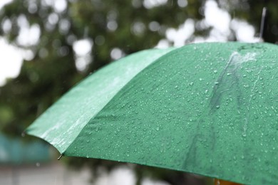 Photo of Green umbrella under heavy rain outdoors, closeup