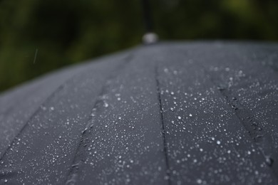 Photo of Black umbrella under heavy rain outdoors, closeup