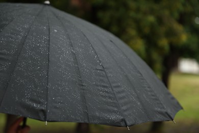 Photo of Person with black umbrella under heavy rain outdoors, closeup