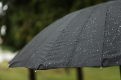 Photo of Black umbrella under heavy rain outdoors, closeup