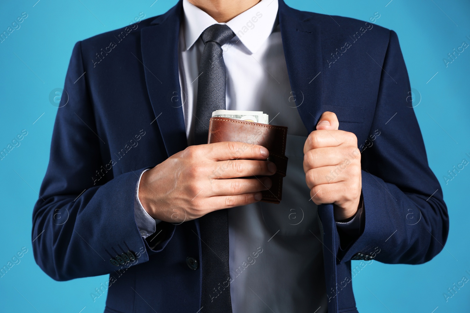 Man putting wallet with dollars into his pocket on blue background, closeup Photo of Man putting wallet with dollars into his pocket on blue background, closeup