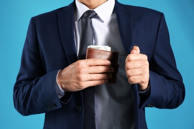 Photo of Man putting wallet with dollars into his pocket on blue background, closeup
