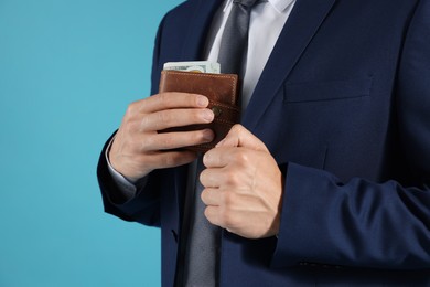 Photo of Man putting wallet with dollars into his pocket on blue background, closeup
