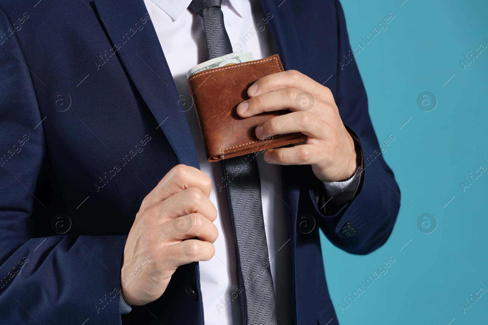 Man putting wallet with dollars into his pocket on blue background, closeup Photo of Man putting wallet with dollars into his pocket on blue background, closeup