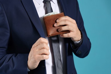 Photo of Man putting wallet with dollars into his pocket on blue background, closeup