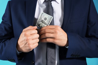 Photo of Man putting dollars in pocket on blue background, closeup