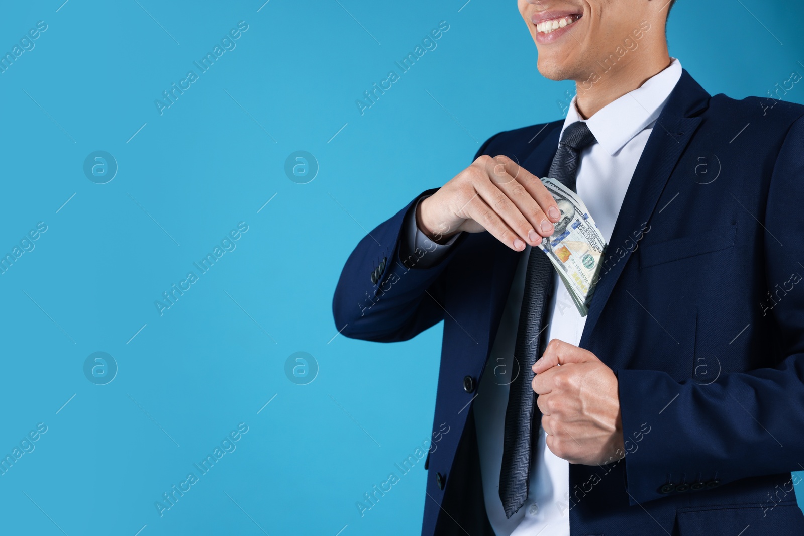 Man putting dollars in pocket on blue background, closeup. Space for text Photo of Man putting dollars in pocket on blue background, closeup. Space for text
