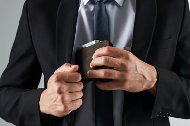 Photo of Man putting wallet with dollars into his pocket on light background, closeup