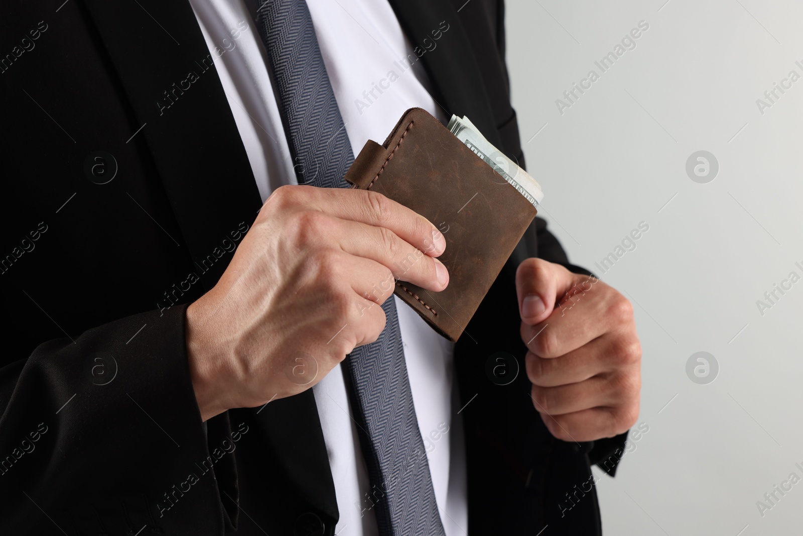 Man putting wallet with dollars into his pocket on light background, closeup Photo of Man putting wallet with dollars into his pocket on light background, closeup