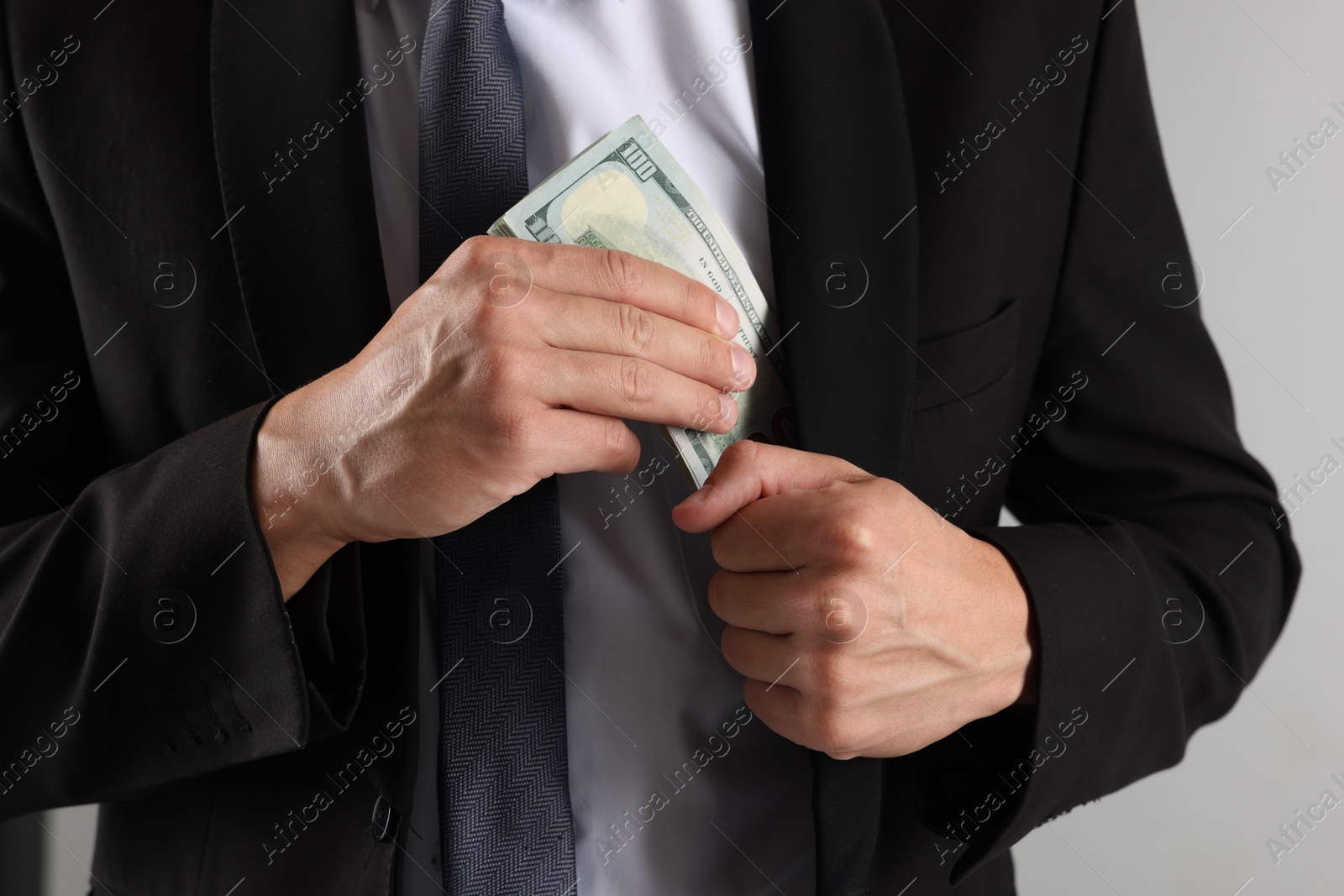 Man putting dollars in pocket on light background, closeup Photo of Man putting dollars in pocket on light background, closeup